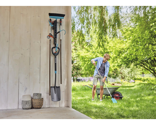 Tuinscene met gereedschaphouder, tuingereedschap en een persoon die in de tuin werkt