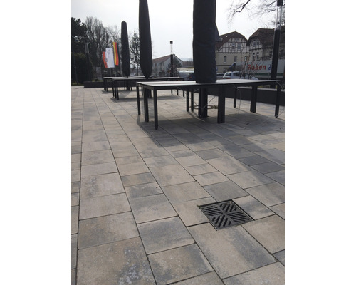 Buitenruimte met straatstenen, afvoerrooster, tafels en parasolhoezen