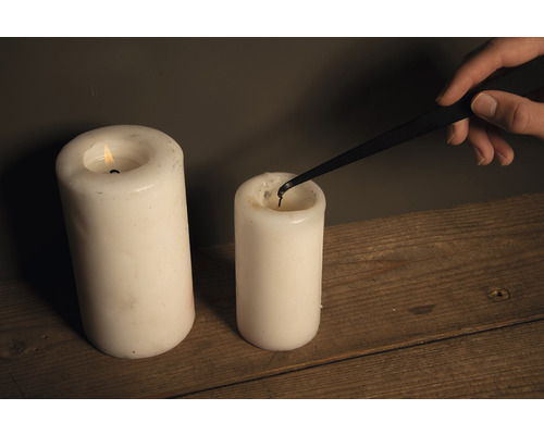 Kaarsendover in gebruik om een stompkaars te doven naast een brandende kaars