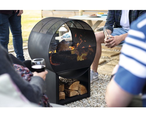 Ronde metalen vuurplaats met houtopslag in de tuin met mensen
