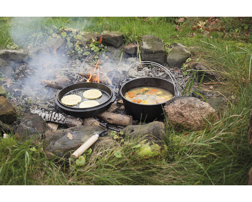 Gietijzeren Dutch Oven en pan boven kampvuur met bereid voedsel.