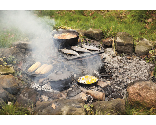 Scène met diverse gerechten die boven een kampvuur worden bereid in gietijzeren potten en pannen