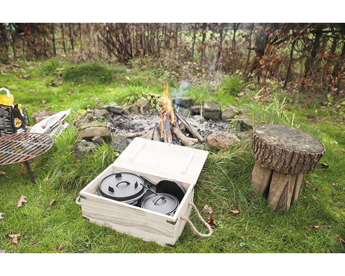 Scene met vuurplaats, houten kruk en Dutch Oven set in een houten kist in de tuin.