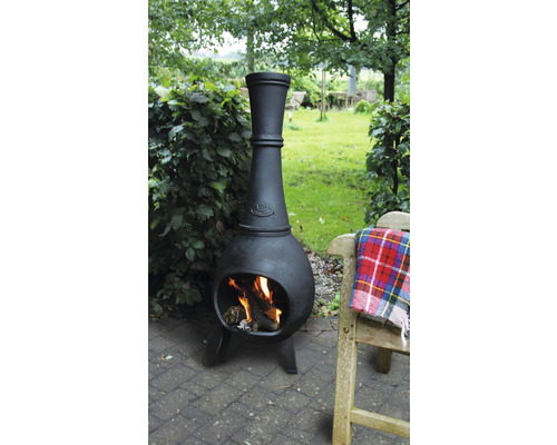 Zwarte tuinhaard met brandend hout naast een houten bank in de tuin.