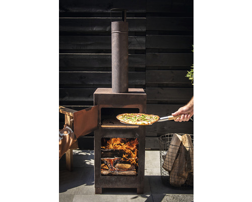 Houtgestookte pizzaoven met open deur, pizza op een pizzaschep en blokken hout in de vuurkamer.