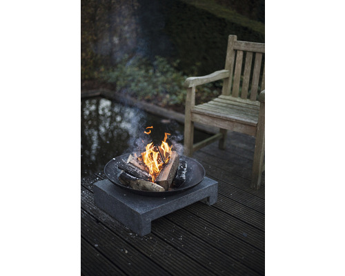 Vuurplaats met hout op stenen voet in de tuin naast houten stoel en vijver