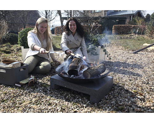 Twee vrouwen zitten buiten bij een vuurkorf en roosteren marshmallows.