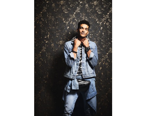 Man met spijkerjas en spijkerbroek voor een gemustreerde wand