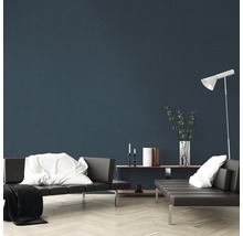 Woonkamer met grijze banken, wit kussen, witte deken, staande lamp en decoraties op een plank voor een blauwe muur