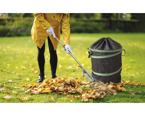Vrouw ruimt bladeren op met een hark en een tuinzak
