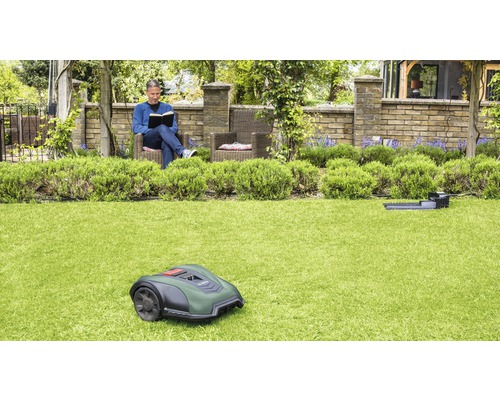 Een man leest in zijn tuin, terwijl een robotmaaier het gras maait.
