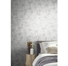 Slaapkamer met grijs betonlook behang, bed en houten bijzettafel.
