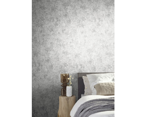 Slaapkamer met grijs betonlook behang, bed en houten bijzettafel.