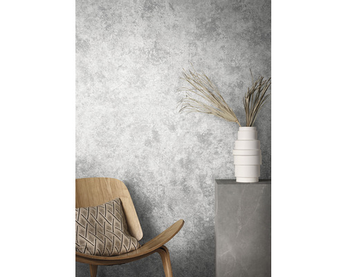 Scene met houten stoel, kussen, vaas en decoratieve takken voor een grijze muur