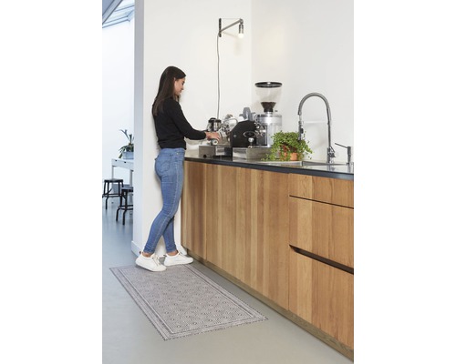 Vrouw bereidt koffie in een lichte keuken met een keukentapijt