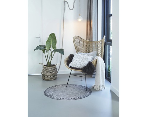 Licht interieur met rotan stoel, plant in mand, rond vloerkleed, kussens en sprei
