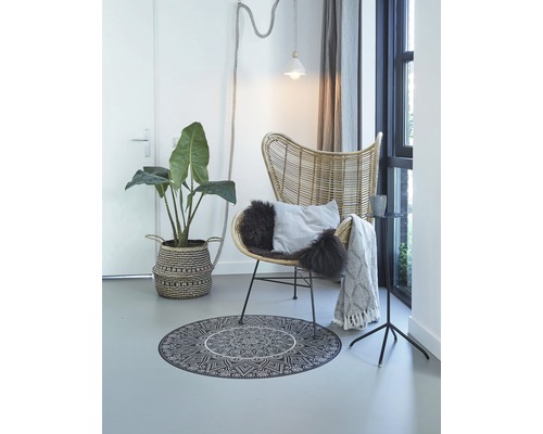 Woonkamer met rotan stoel, rond tapijt met mandala motief en kamerplant in mand