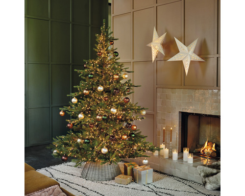 Versierde kerstboom met lichtjes en ballen in de woonkamer naast een open haard.