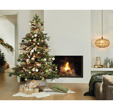 Feestelijk versierde kerstboom naast een open haard in een lichte woonkamer.