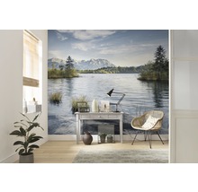 Woonkamer met fotobehang met een meer en bergen, plus een tafel, een lamp en een stoel.