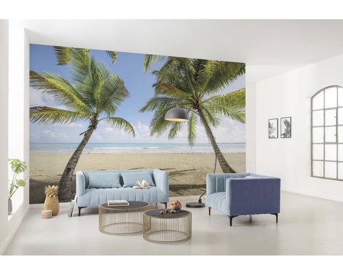 Woonkamer met fotobehang dat een tropisch tafereel met palmbomen en strand laat zien, met meubels zoals een bank en fauteuils.