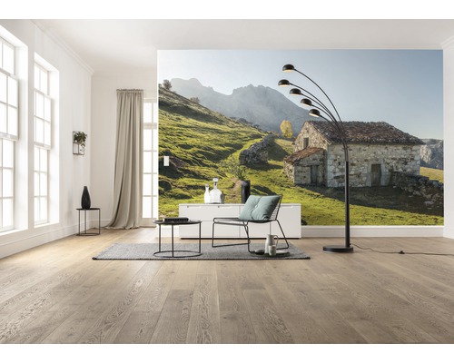 Woonkamer met fotobehang van een stenen huis in een groen heuvellandschap