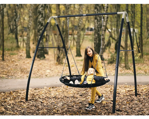 Moeder duwt kind op een schommelnest met stalen frame in de tuin