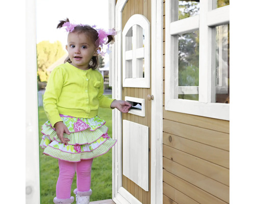 Een jong meisje steekt een brief in de brievenbus van een houten speelhuis.