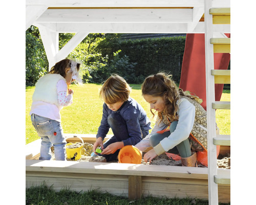 Drie kinderen spelen in de zandbak onder een speeltoren in de tuin.