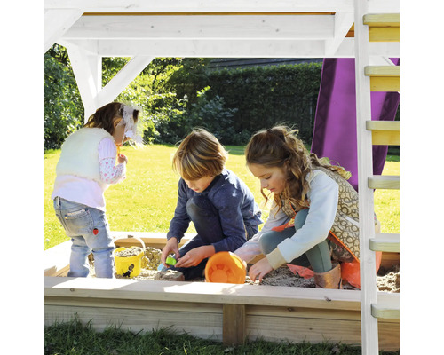 Kinderen spelen in een zandbak met dak en ladder in de tuin.