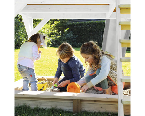 Kinderen spelen in de zandbak met dak en ladder in de tuin.