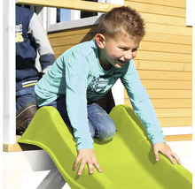 Jongen glijdt van een groene glijbaan in een speelhuisje