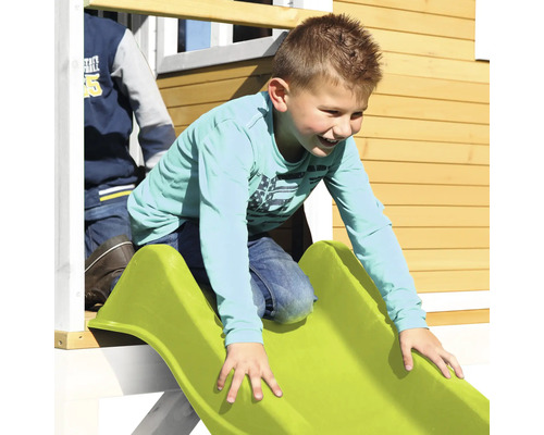 Jongen glijdt van een groene glijbaan in een speelhuisje