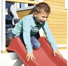 Jongen glijdt van een rode kinderglijbaan aan een speelhuisje.