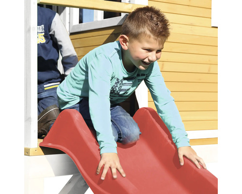 Jongen glijdt van een rode kinderglijbaan aan een speelhuisje.