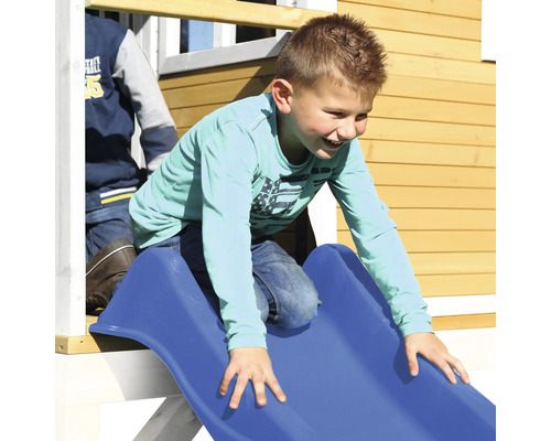 Jonge glijdt van een blauwe glijbaan aan een speelhuis