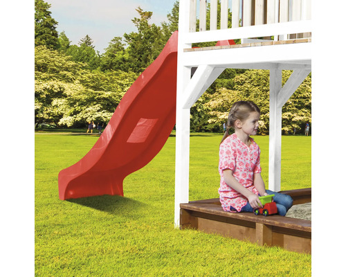 Kind zit in de zandbak onder een speeltoren met glijbaan.