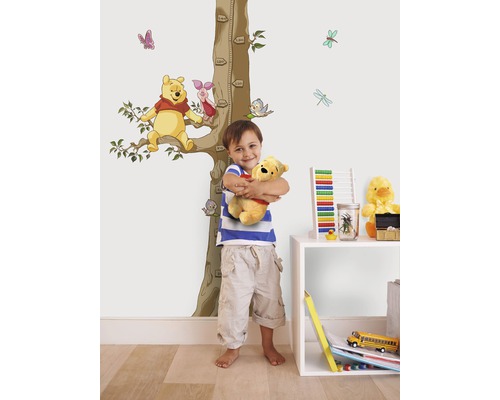 Jongen knuffelt Winnie de Poeh knuffel voor een muur met Winnie de Poeh muursticker en groeimeting.