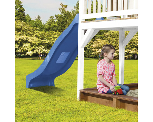 Meisje zit in een zandbak onder een speeltoren met glijbaan op een gazon