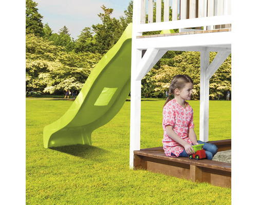 Kind zit in zandbak onder speeltoren met glijbaan in de tuin