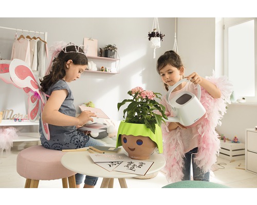 Twee meisjes spelen in een kamer met een plant in een pot met een gezicht en een gieter.