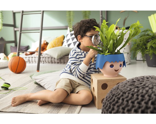 Jonge onderzoekt plant in pot met vergrootglas in een kamer.