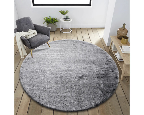 Rond grijs vloerkleed in woonkamer met fauteuil en bijzettafel.