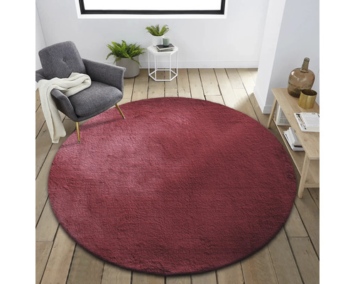 Interieur met rond, bordeauxrood tapijt, fauteuil, bijzettafel en houten plank