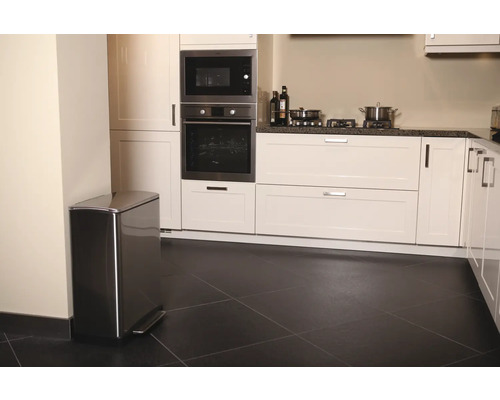 Keuken met roestvrijstalen pedaalemmer, witte kasten en zwarte vloertegels.