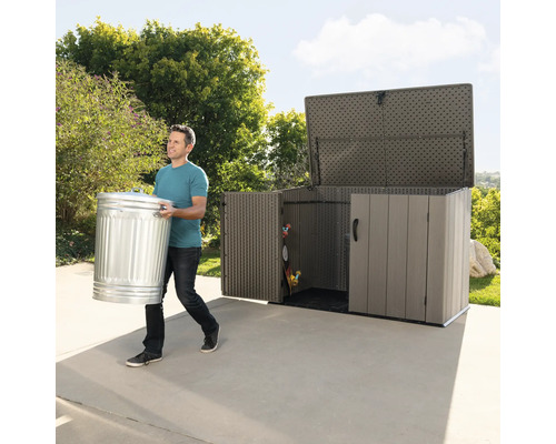 Man draagt een vuilnisemmer naar een tuinkast in de tuin.