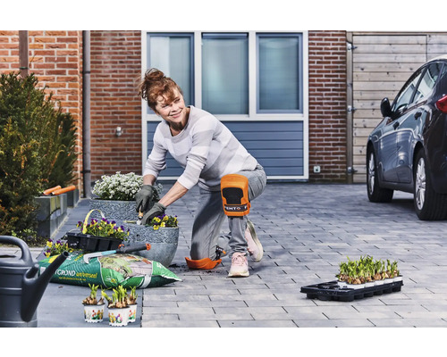 Vrouw plant bloemen in potten in de tuin met kniebeschermers