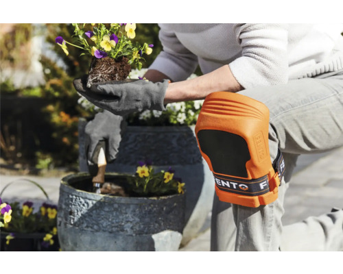 Persoon met kniebeschermers en tuinhandschoenen plant bloemen in een pot