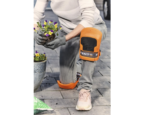 Een persoon met kniebeschermers plant bloemen in de tuin.