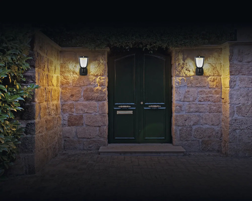Verlichte ingang met twee wandlampen op een stenen muur.